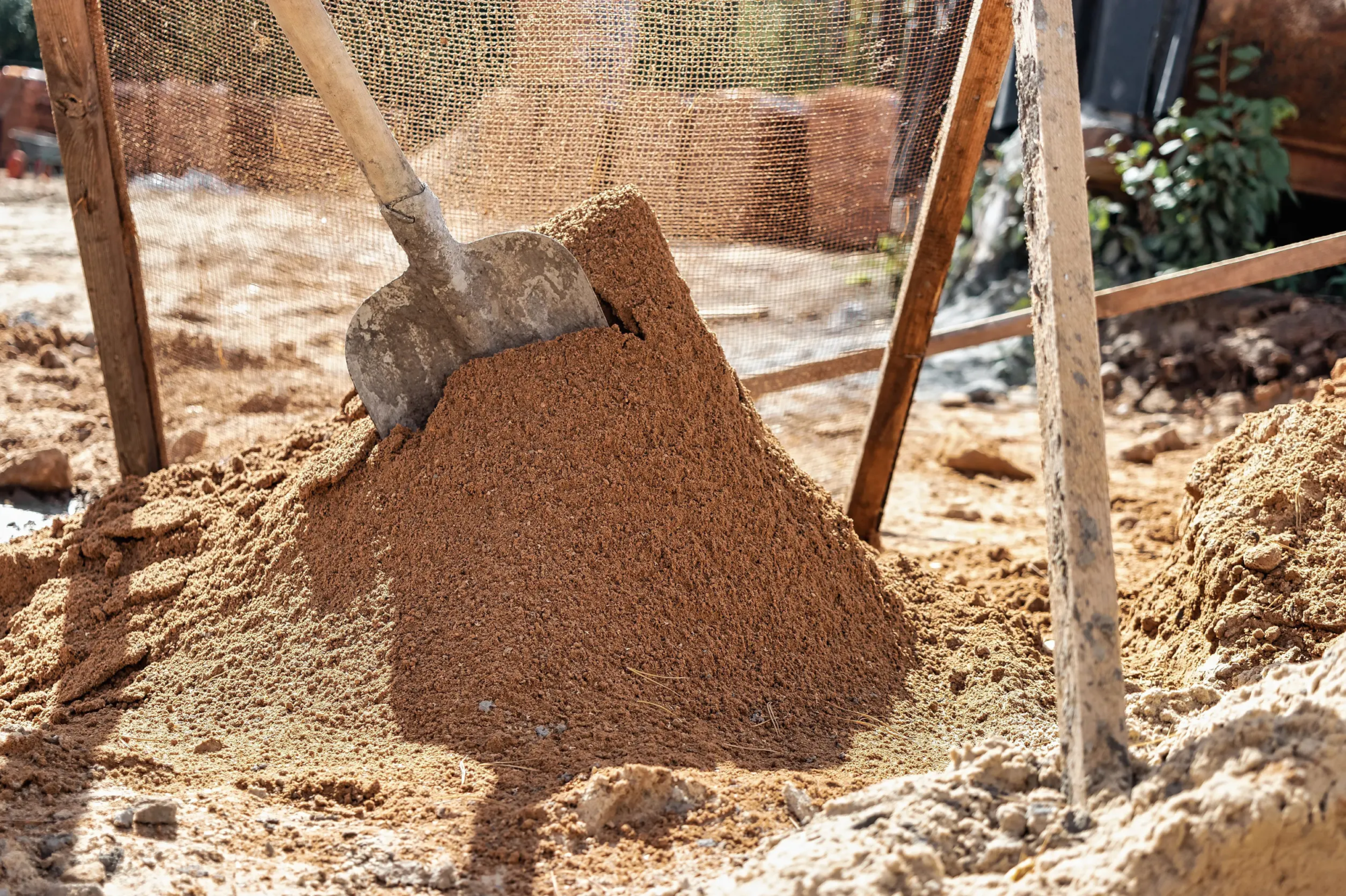 A spade standing upright embedded into building sand that is being sifter for mortar