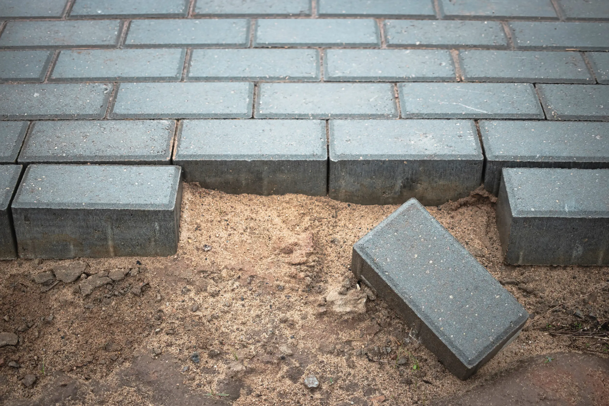 A close up shot of a drive way being paved, thick neatly lines grey bricks and sand where new bricks are to be paved