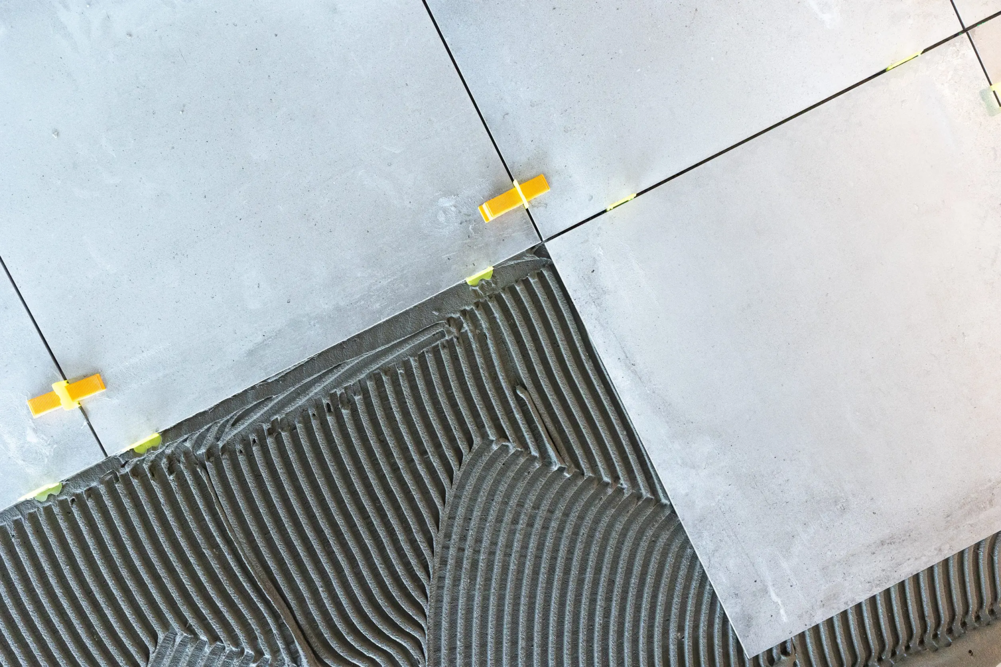 A close up shot of white tiles with leveling pegs and a section prepared with fresh tile adhesive for a new tile